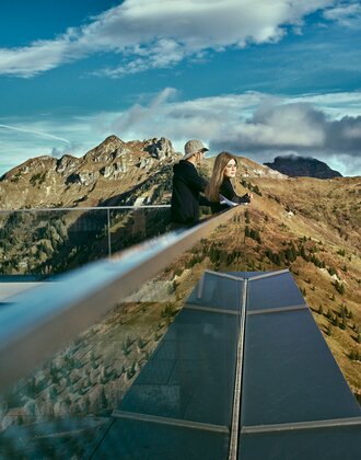 Zwei Personen blicken vom modernen Aussichtspunkt am Kieserl in Großarl über die herbstliche Berglandschaft der Alpen. | © Großarler Bergbahnen