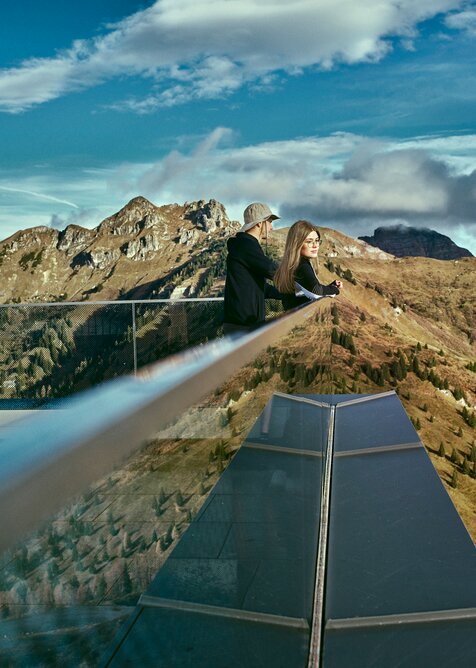 Zwei Personen blicken vom modernen Aussichtspunkt am Kieserl in Großarl über die herbstliche Berglandschaft der Alpen. | © Großarler Bergbahnen