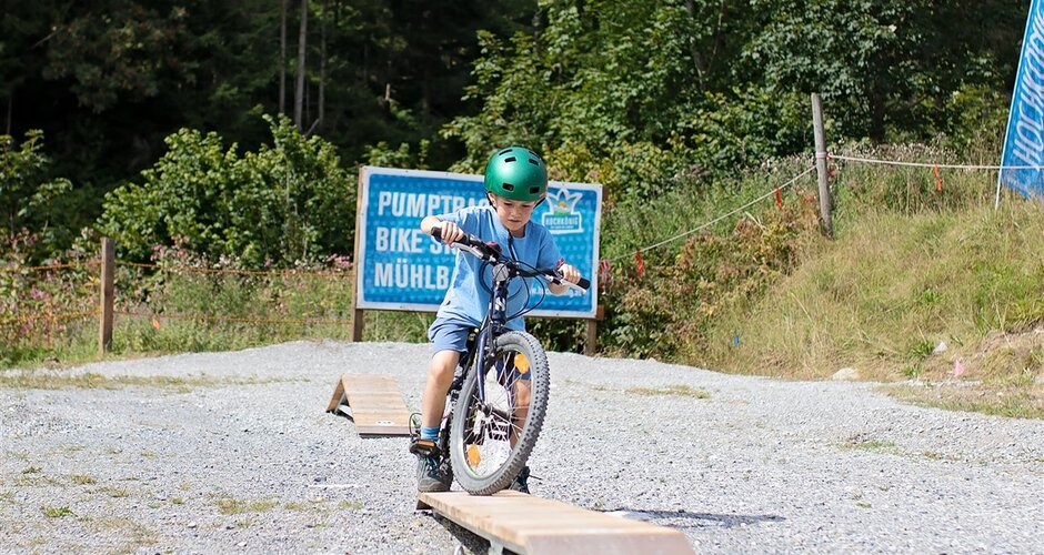 Kind mit grünem Helm balanciert auf Holzrampe im Pumptrack & Skill Area Mühlbach
