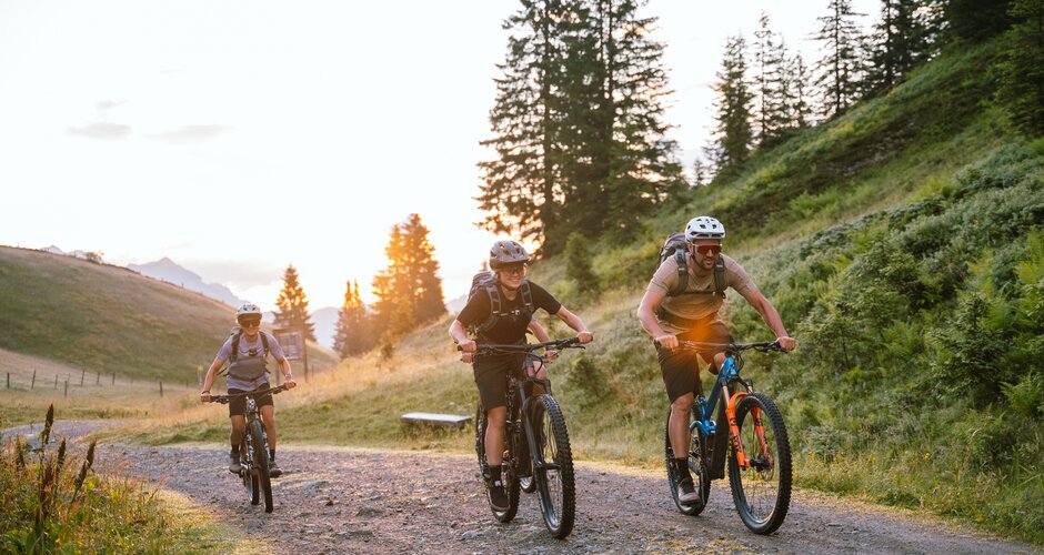 Drei Mountainbiker fahren auf einem Schotterweg in Mühlbach bei Sonnenuntergang nahe der Karbachalmbahn. | © Hochkönig Bergbahnen
