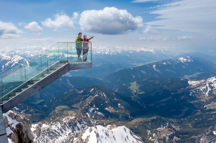 Dachstein Stairway to Heaven with breathtaking panorama | © Harald Steiner Two people stand on the glass Skywalk at Dachstein, overlooking snow-covered peaks and a vast mountain landscape. | © Harald Steiner