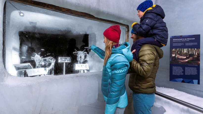 Familie mit Kind betrachtet Eisfiguren hinter Glas im Eispalast Dachstein; Informationstafel zur Almwirtschaft in der Römerzeit. | © Harald Steiner