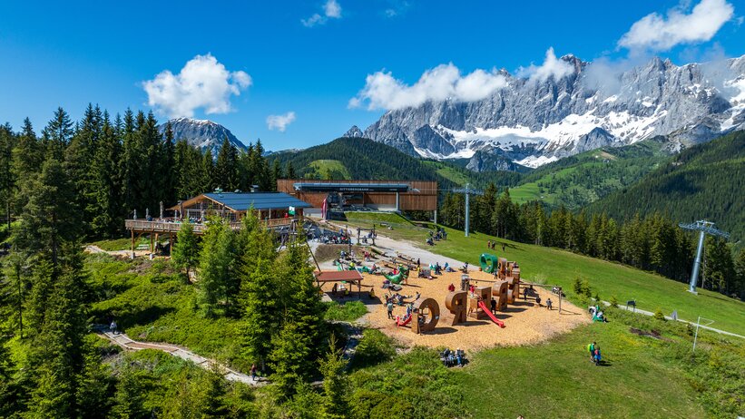 Weitläufiger Spielplatz mit Holzelementen, Rutschen und Kletterstrukturen vor einem Bergrestaurant und der Rittisberg-Seilbahn. | © Erlebnis Rittisberg