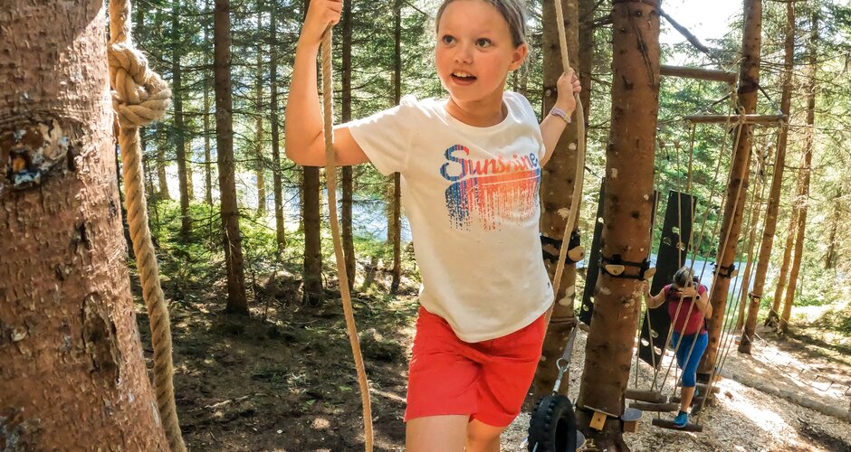 Mädchen balanciert auf Reifen im Waldseilgarten, weitere Kinder klettern im Hintergrund. | © Shuttleberg