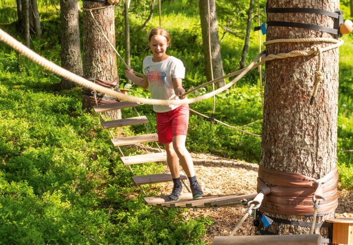 Klettern im Hochseilgarten am Shuttleberg | © Shuttleberg Mädchen überquert Hängebrücke im Waldseilgarten bei sonnigem Wetter. | © Shuttleberg