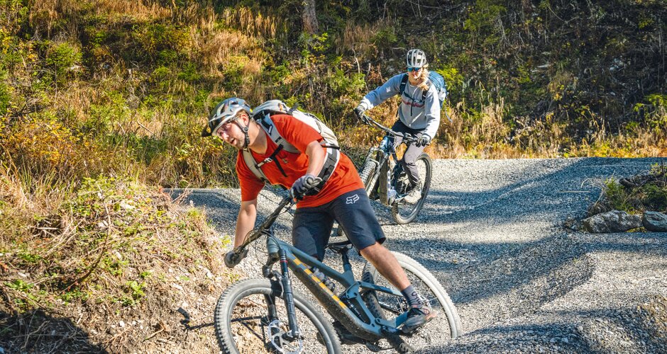 Zwei Mountainbiker fahren in Schräglage durch eine enge Kurve auf dem Schottertrail. | © Shuttleberg
