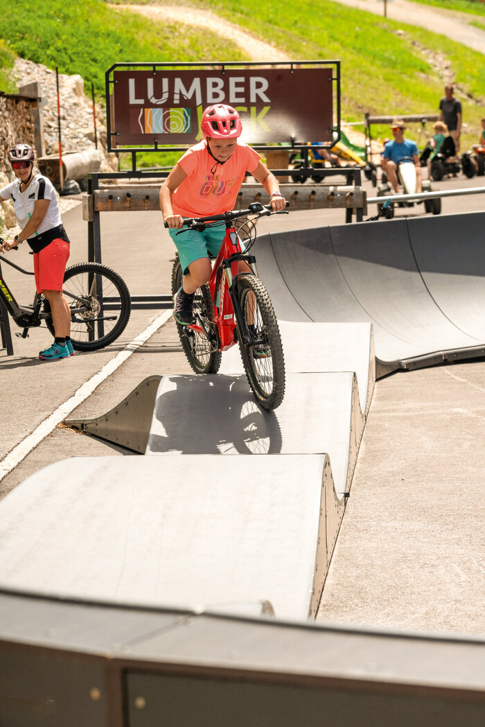 Pumptrack-Abenteuer in Shuttleberg Flachauwinkl | © Shuttleberg Kind fährt auf rotem Mountainbike mit Helm und pinkem Shirt über Pumptrack-Wellen | © Shuttleberg