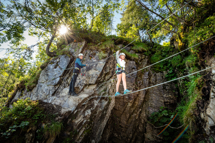 Climbing adventure with rope safety at Geisterberg | © Snow Space Salzburg, Christoph Huber Two kids with helmets and harnesses on rope bridge at rock wall, sunny weather, trees and cliffs in background. | © Snow Space Salzburg, Christoph Huber