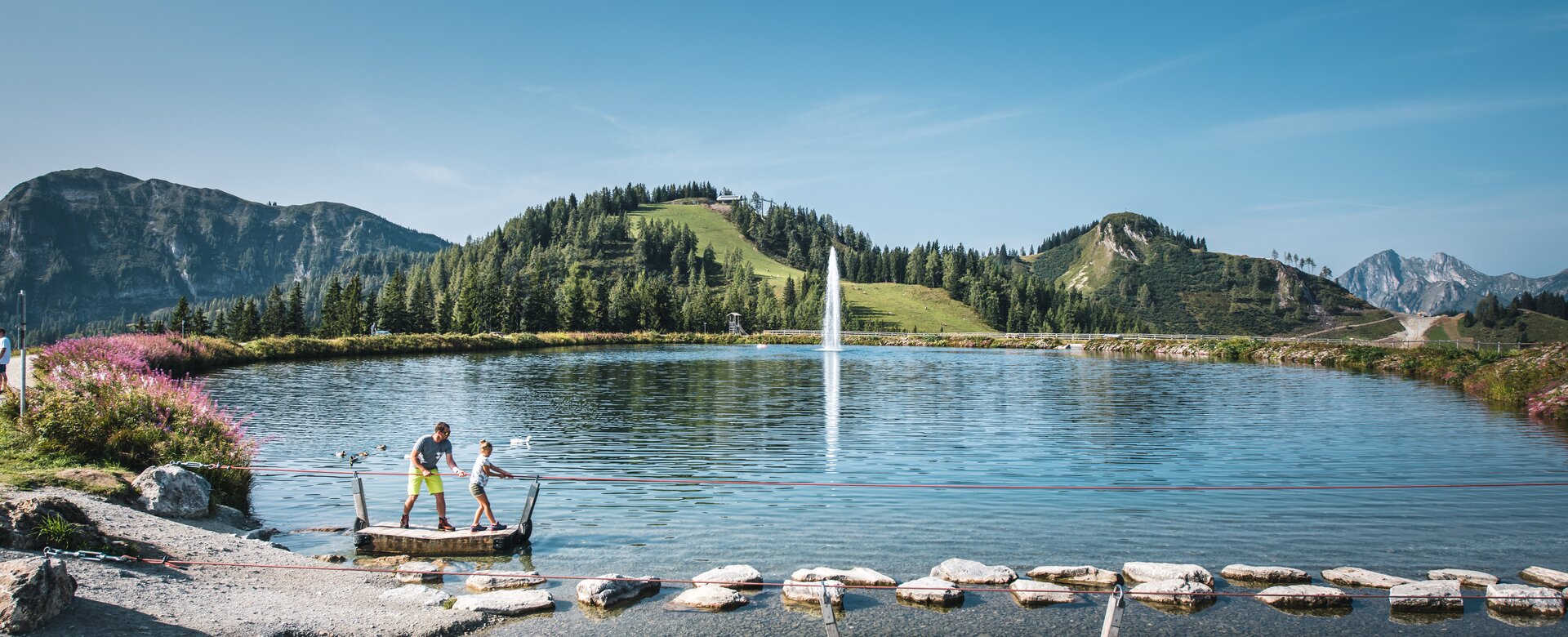 Ein Vater und seine Tochter stehen auf einem Floß und ziehen sich an einem Seil auf das gegenüber liegende Ufer | © Christian Schartner