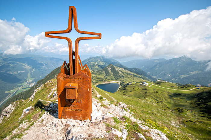 Gipfelkreuz auf dem Schwarzkopf bei der 4-Gipfel-Tour Zauchensee | © Zauchensee Liftgesellschaft Rostiges Gipfelkreuz am Schwarzkopf mit Fernblick über Alpenlandschaft, Bergsee und Wanderwege bei Zauchensee. | © Zauchensee Liftgesellschaft
