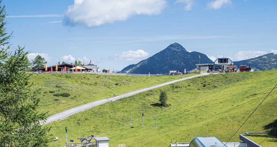 View of Gamskogelbahn top station, hut, walking path and alpine landscape in Zauchensee under clear summer skies. | © Matthias Fritzenwallner