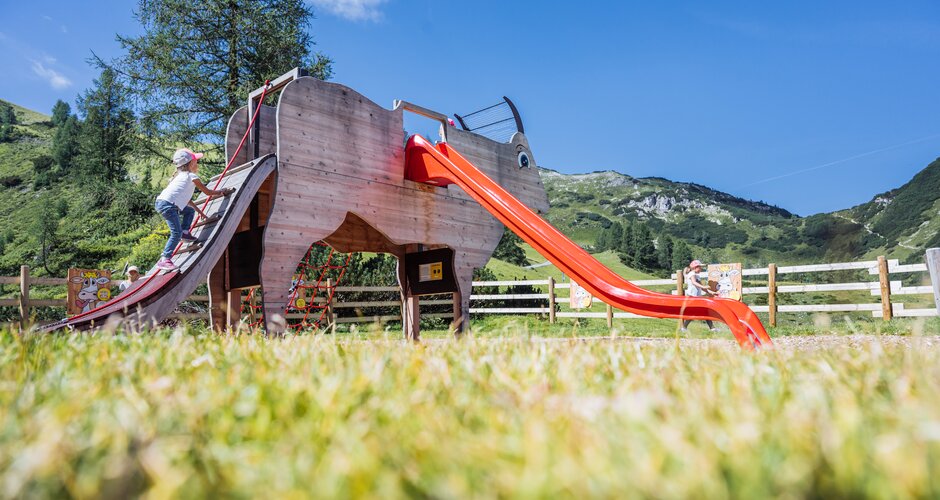 Girl climbs ramp of a cow-shaped play structure with red slide at the children’s playground in Zauchensee. | © Zauchensee Liftgesellschaft