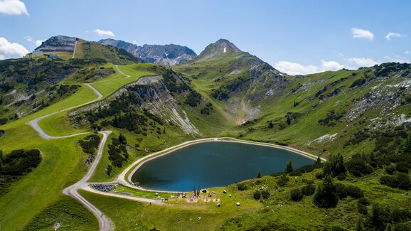 Reservoir lake with circular hiking path, play station and alpine scenery in the green summer mountains of Zauchensee