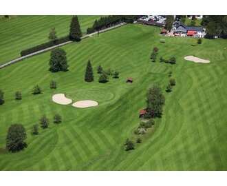 Luftaufnahme vom Golfclub Gastein mit gepflegten Fairways, Sandbunkern, kleinen Hütten und Clubhaus im Hintergrund. | © Golf Club Gastein