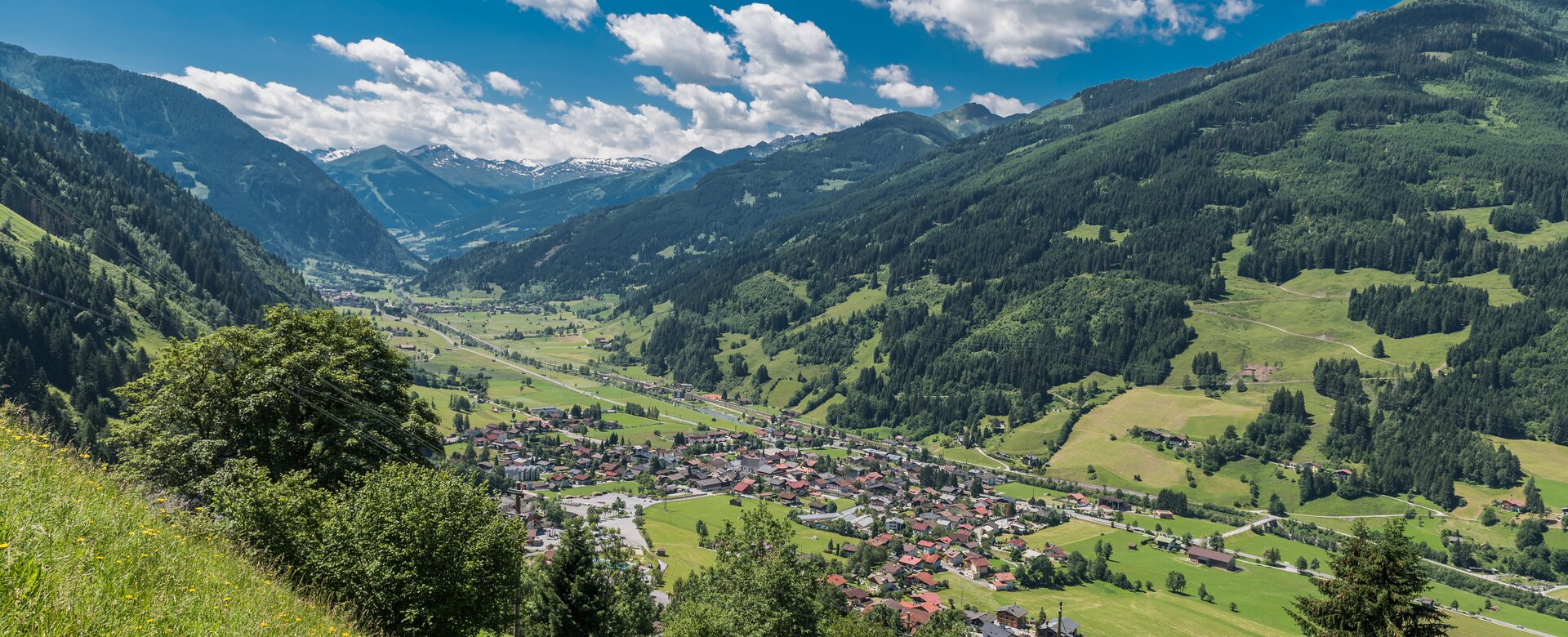 Weitblick auf Dorfgastein mit grünen Wiesen, bewaldeten Bergen und Gasteinertal unter blauem Himmel | © Gasteinertal Tourismus GmbH