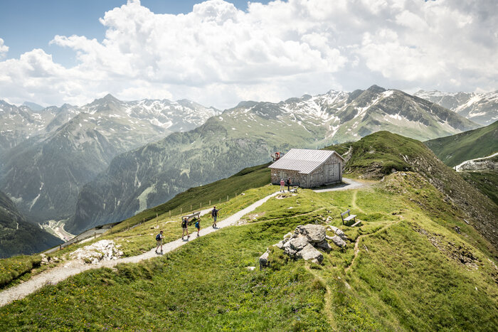 Hikers at mountain hut with panoramic view of the Gastein Alps | © Gasteinertal Tourismus GmbH Group of hikers on mountain trail near wooden hut with view of snow-covered peaks in Gastein | © Gasteinertal Tourismus GmbH