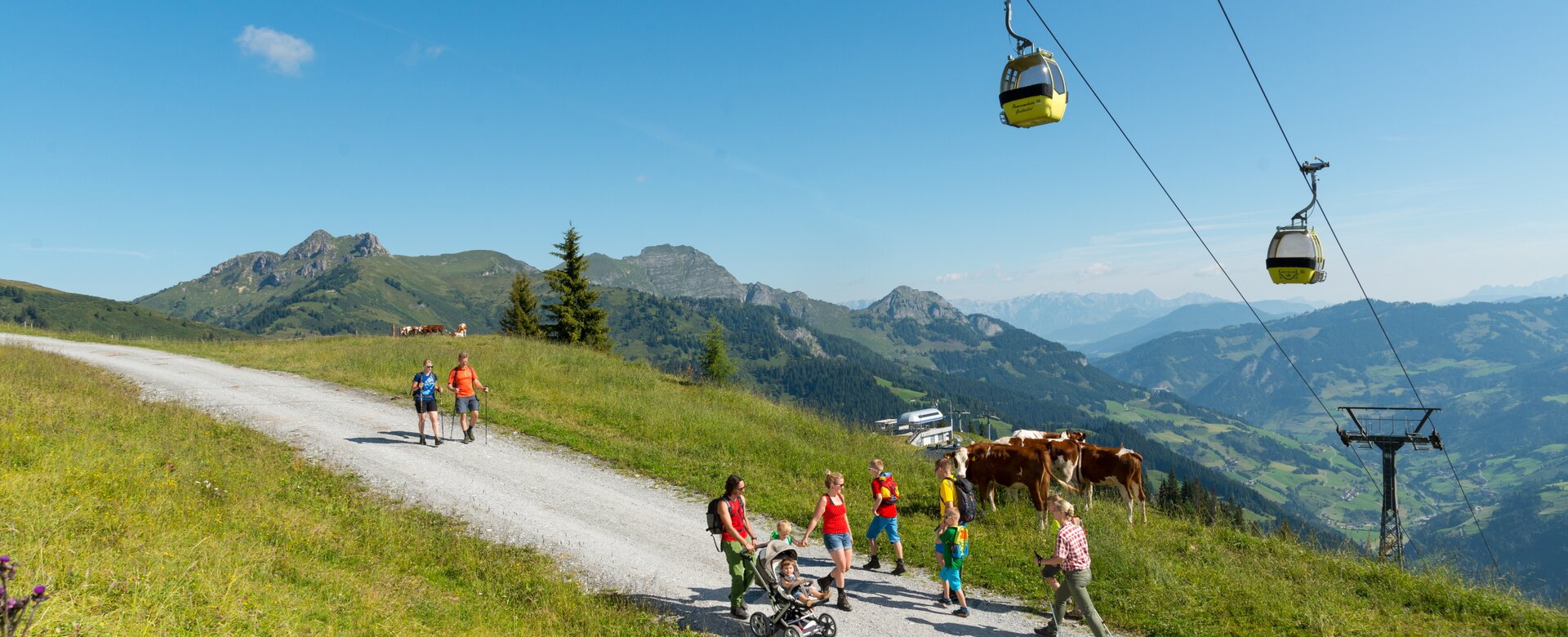 Menschen spazieren auf einer Schotterstraße unter einer Kabinenseilbahn den Berg hinauf | © Gruber Michael