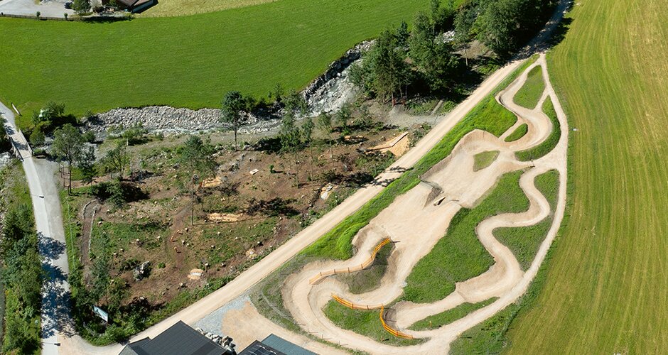 Luftaufnahme eines Mountainbikeparks mit geschwungenen, unbefestigten Trails in grüner Landschaft | © Sport Panorama