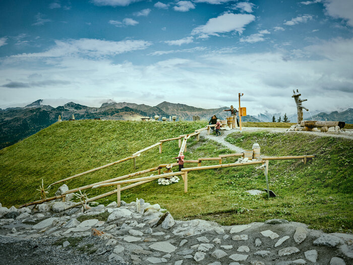 Kinder spielen an Wasserstationen auf Erlebnisweg im Großarltal mit Holzrinnen, Wiese und Bergpanorama | © Chris Rogl