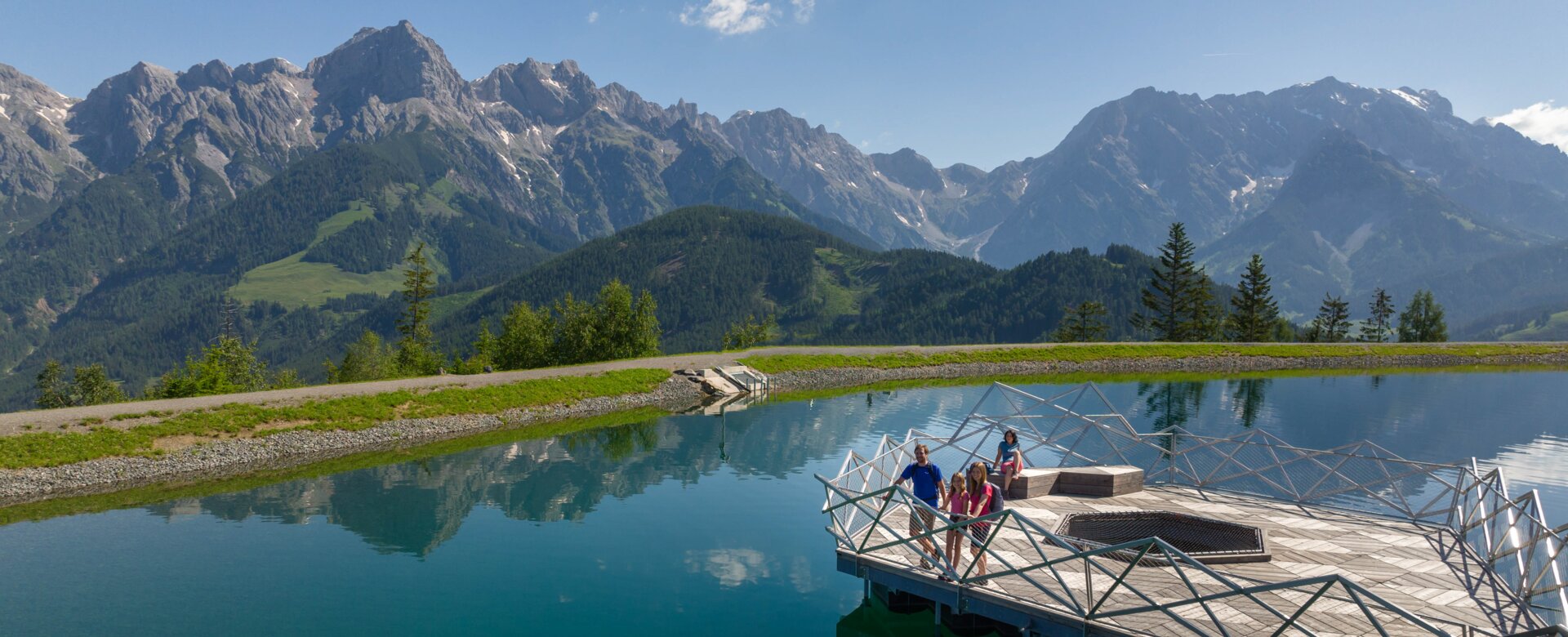 Familie auf Holzplattform am Prinzensee in Maria Alm, klares Wasser, Bergpanorama Hochkönig im Hintergrund | © Roland Haschka