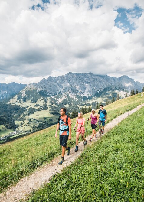 Fünf Wanderer gehen auf Bergpfad oberhalb eines grünen Tals mit Blick auf die markanten Felsen des Hochkönig-Massivs | © Hochkönig Tourismus GmbH