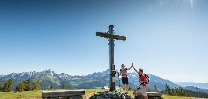 Zwei Personen stehen auf einem Plateau bei einem Gipfelkreuz und geben sich ein High Five | © Tourismusverband Radstadt/Lorenz Masser