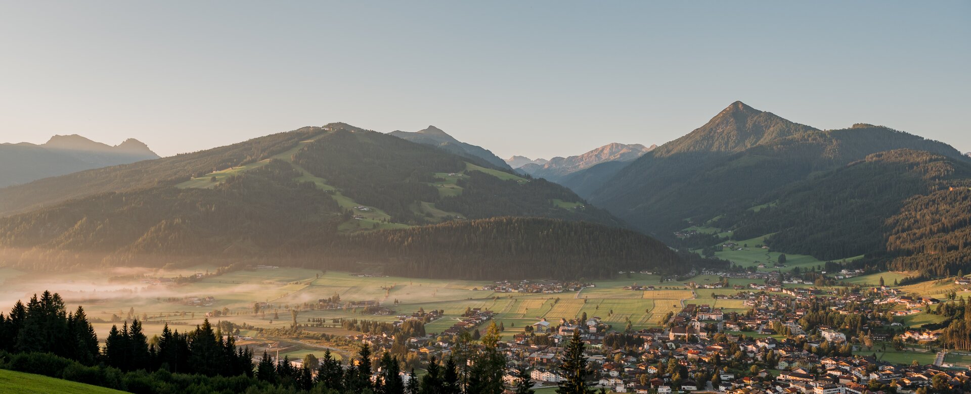 Blick auf ein Dorf im Tal und die Sonne beginnt gerade einige Flecken zu beleuchten und den morgendlichen Nebel zu vertreiben | © Matthias Fritzenwallner