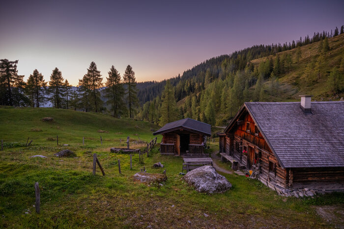 Almsommer in Altenmarkt-Zauchensee | © Christian Schartner Eine urige Hütte aus Holz steht auf der Seite und wird von einer Almwiese und Bäumen umrahmt während die Sonne gerade untergegangen ist. | © Christian Schartner