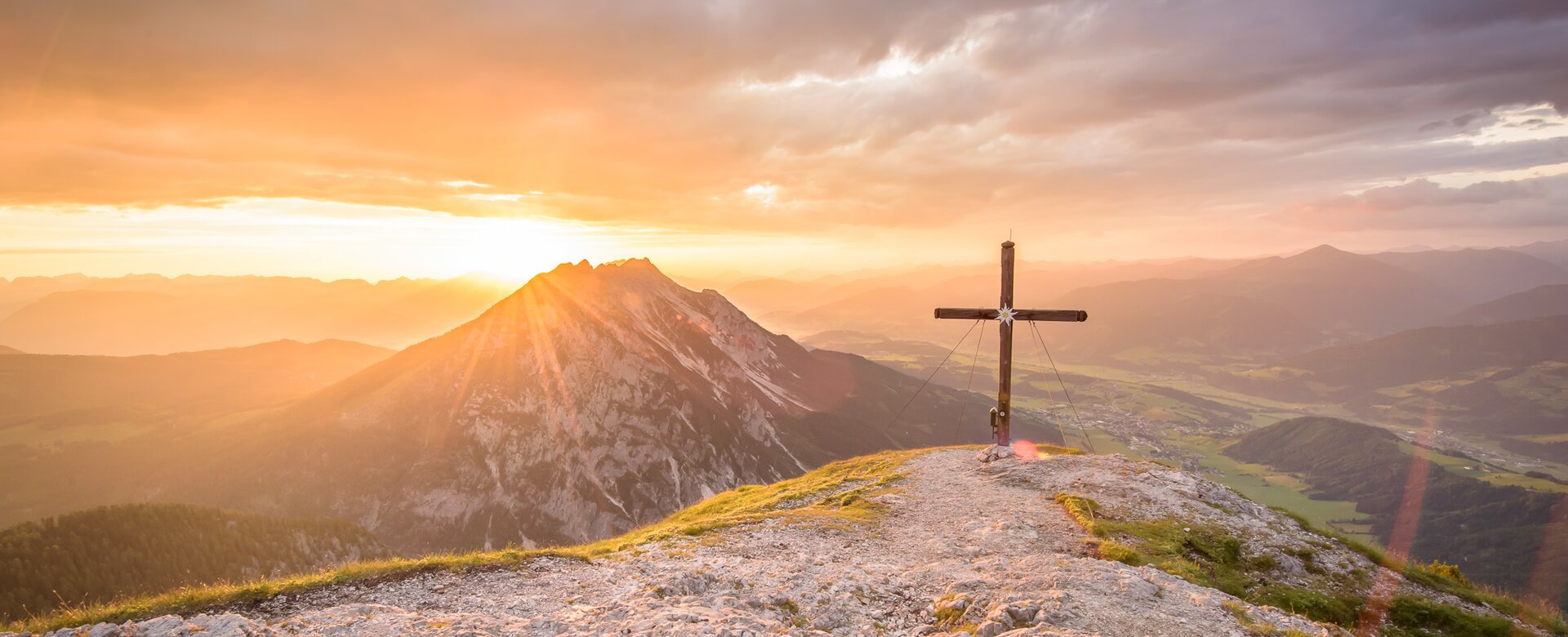 Gipfelkreuz bei Sonnenaufgang mit Blick über das Gröbminger Land, Berglandschaft in goldenes Morgenlicht getaucht | © Christoph Huber