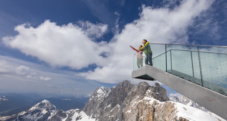 Zwei Personen stehen auf einer gläsernen Aussichtsplattform über schneebedeckten Felsen des Dachsteinmassivs | © Harald Steiner