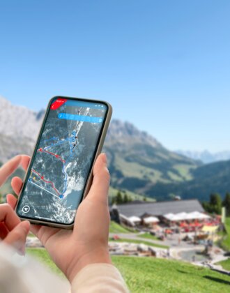 Digital route planning via app in Ski amadé with gondola and peaks Person holds smartphone with interactive trail map, background shows gondola, huts and mountain panorama in Ski amadé.