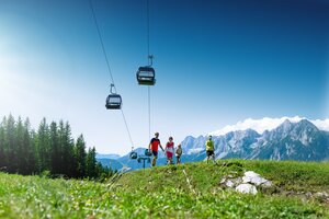 Familie wandert auf Almwiese mit Seilbahn und Alpenpanorama im Hintergrund