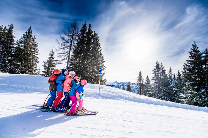 Ski amadé Minis Week – kids having fun on the slopes Six children in colorful ski outfits ski closely together down the slope, smiling and enjoying the snow.