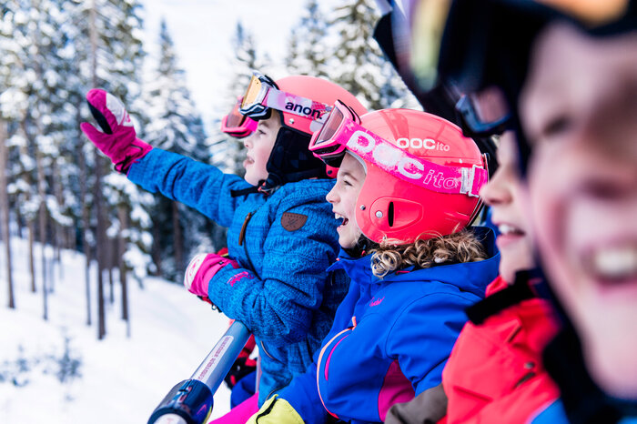 Ski amadé Minis Week – kids on the chairlift Kids with colorful helmets and ski goggles ride the chairlift, smiling as they move through the snowy mountain landscape.