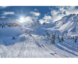 Skipiste mit orangefarbenen Sesselliften, Sonne und verschneiten Bergen am Hauser Kaibling.