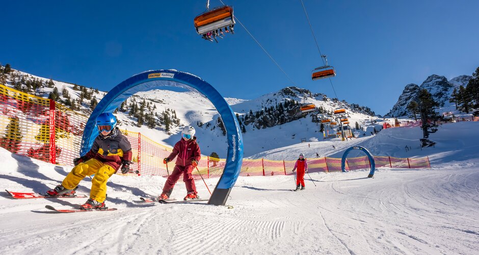 Kids skiing through blue gates on the XXL funslope at Hauser Kaibling in bright sunshine. | © Hauser Kaibling