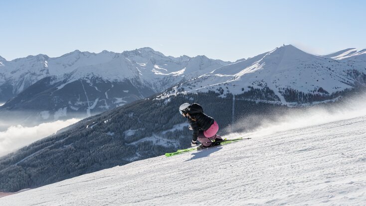 Skifahrerin in Kurve auf Piste mit Blick auf verschneite Wälder und Berge | © Simon Hutter