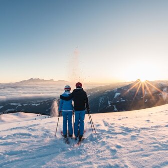 Zwei Skifahrer genießen den Sonnenaufgang mit Blick auf verschneite Berge und Täler