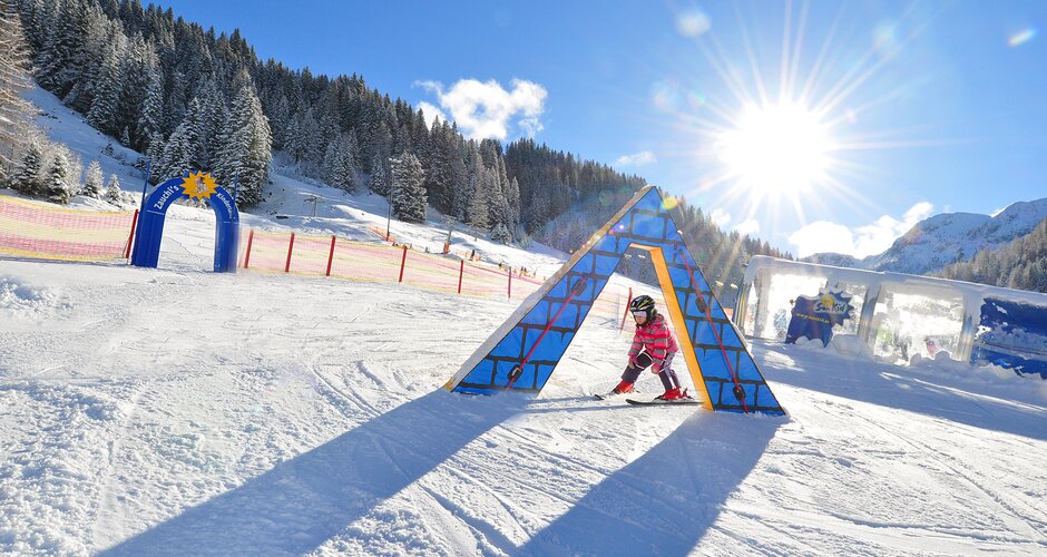 Kind mit Ski fährt durch buntes Hindernis im Kinderland Zauchensee bei Sonnenschein