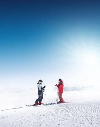 Zwei Skifahrer stehen auf frisch präparierter Piste in Ski amadé mit Blick über wolkenverhangenes Tal