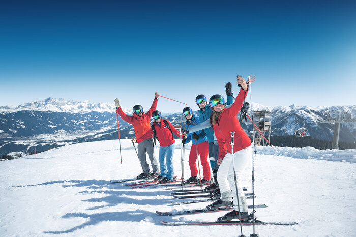 Gruppen-Selfie beim Skifahren in Ski amadé Sechs Skifahrer machen bei Sonnenschein auf der Piste ein fröhliches Gruppen-Selfie