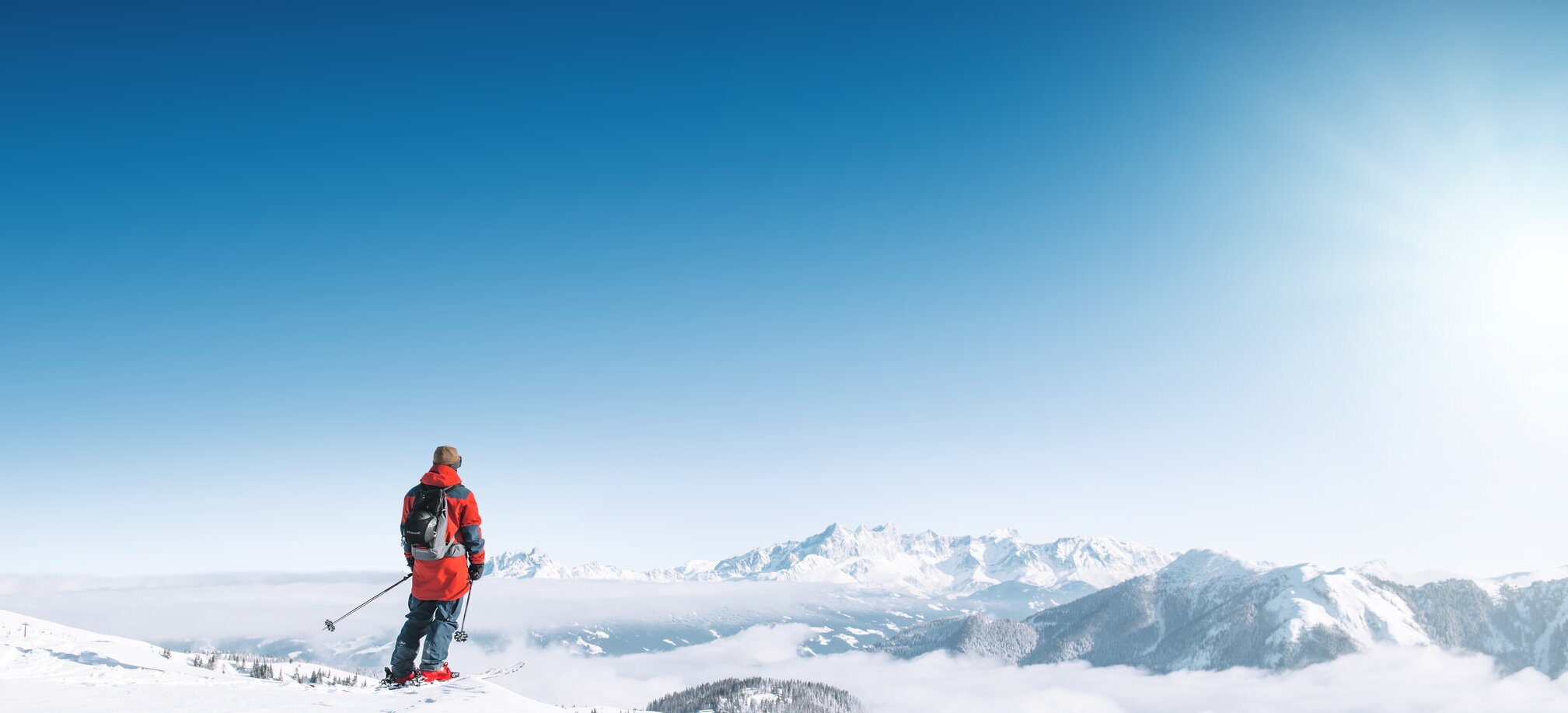 Ein Skifahrer blickt auf verschneite Berge und ein weites Nebelmeer bei klarem Sonnenschein