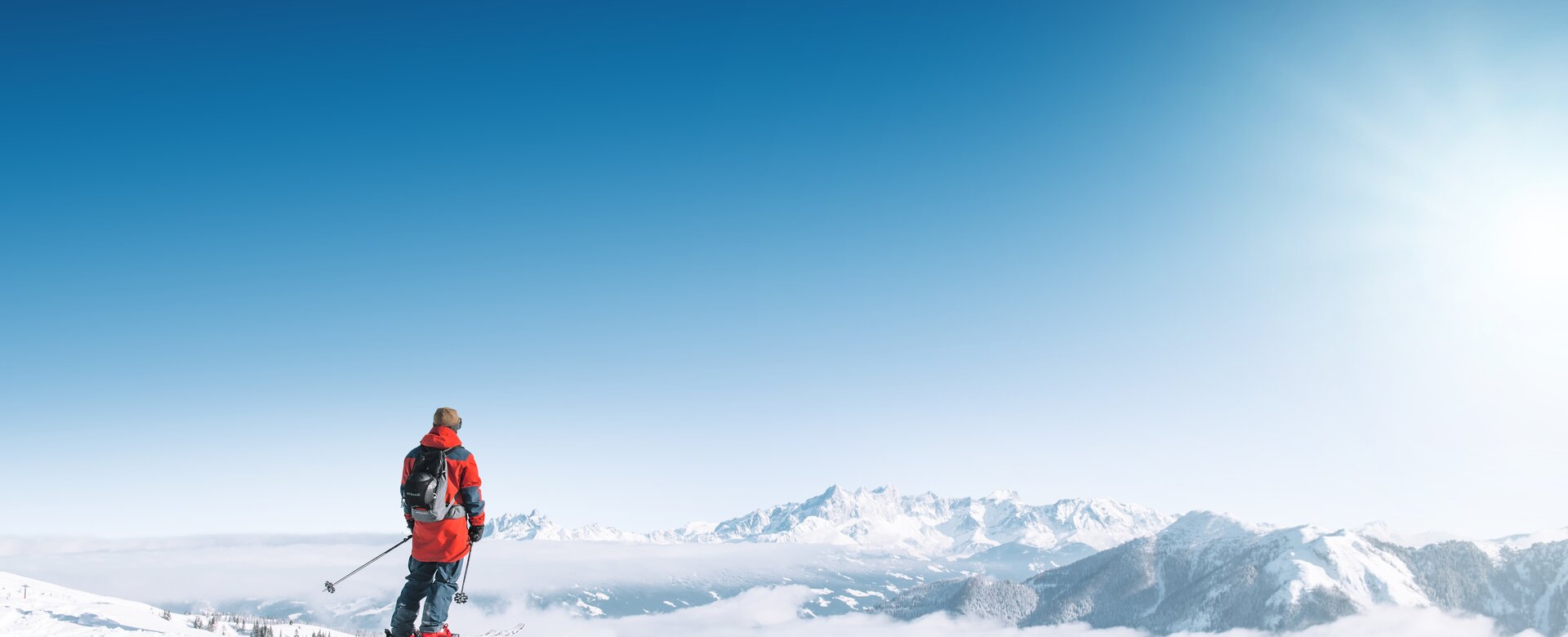 Ein Skifahrer blickt auf verschneite Berge und ein weites Nebelmeer bei klarem Sonnenschein