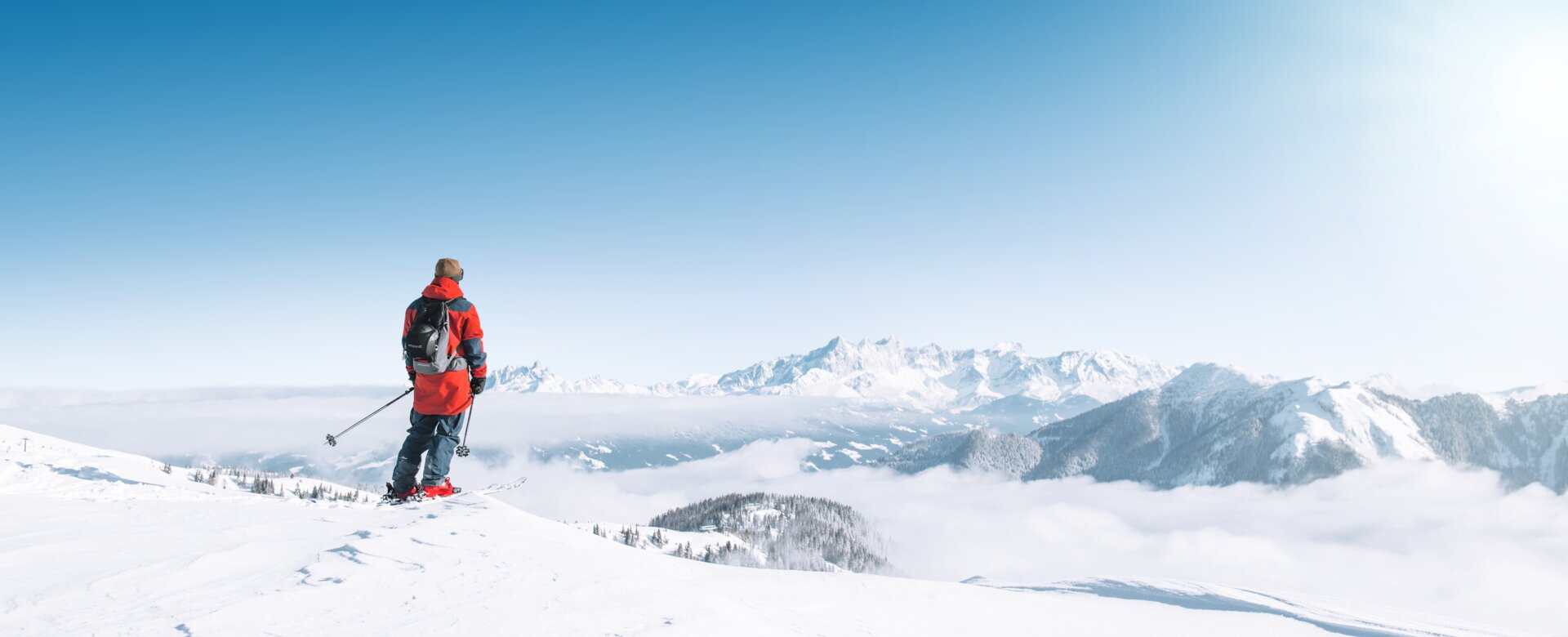 Ein Skifahrer blickt auf verschneite Berge und ein weites Nebelmeer bei klarem Sonnenschein