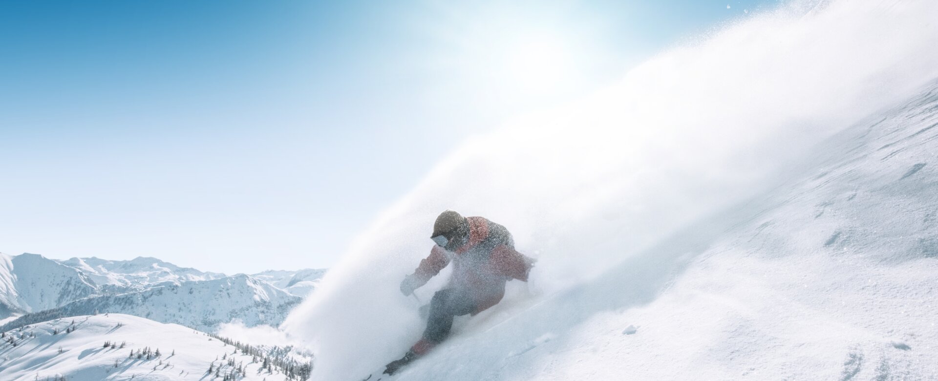 Snowboarder fährt im Tiefschnee eine steile Hangflanke hinab, Pulverschnee spritzt auf