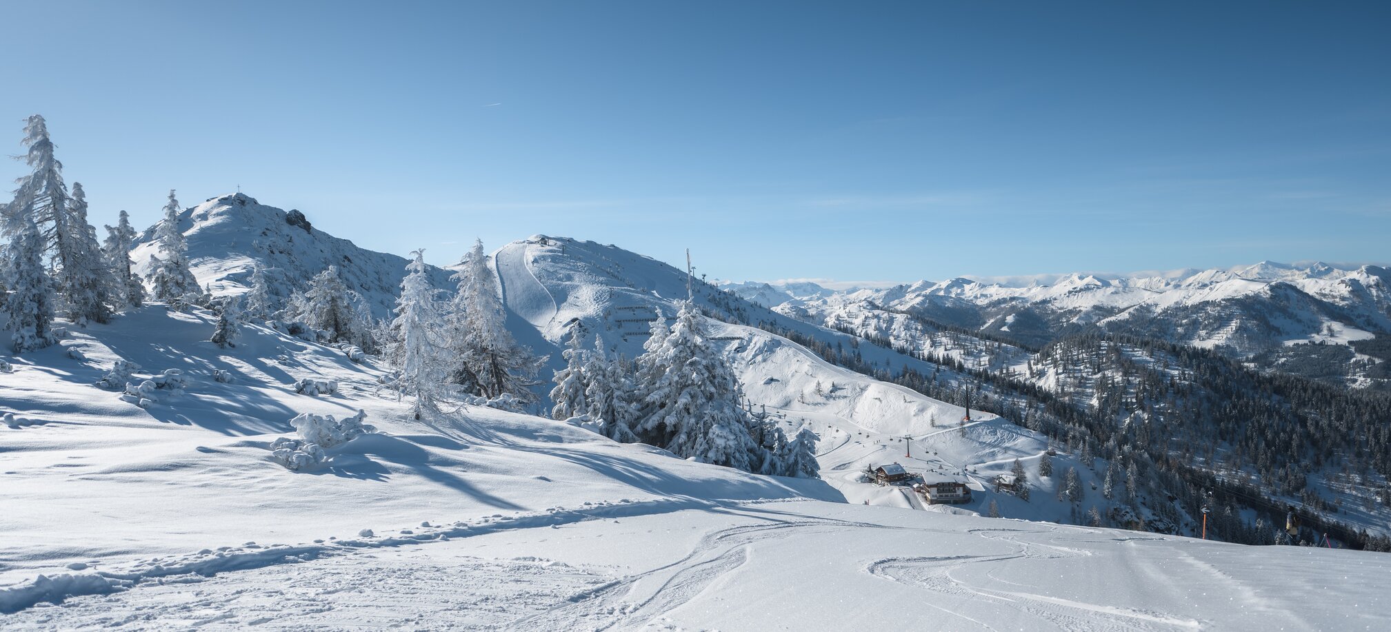 Snow-covered hills with ski tracks under a clear blue sky. | © Ski amadé