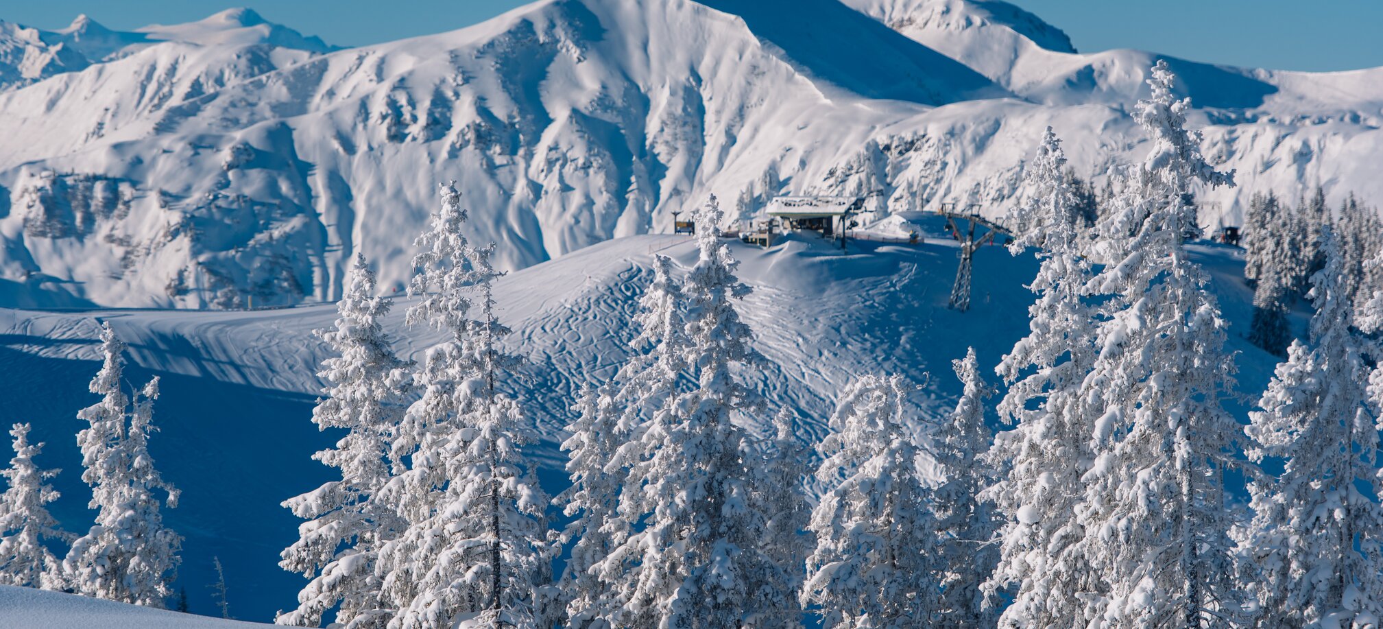 Verschneite Bäume vor majestätischen Bergen und einer Liftstation. | © Ski amadé