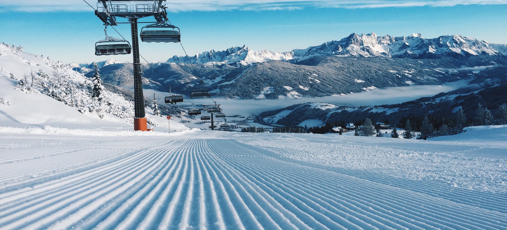 Freshly groomed slope with a chairlift and snow-covered mountains. | © Ski amadé