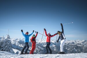 Vier Freunde in Skiausrüstung stehen auf der Piste und Strecken die Arme freudvoll in die Höhe. | © Ski amadé