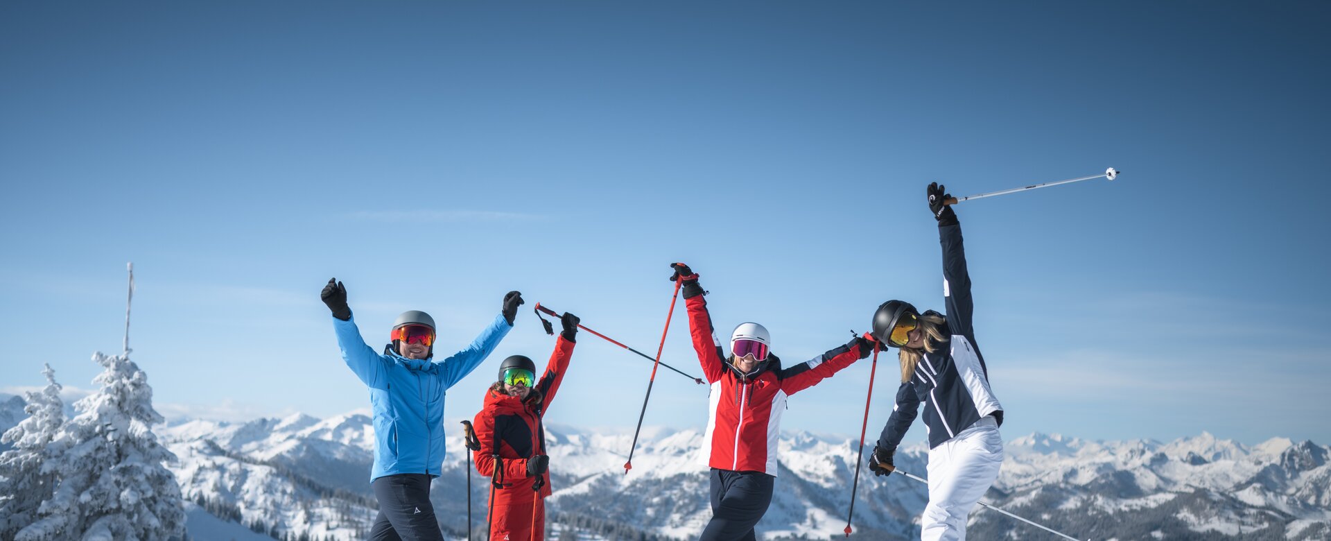 Vier Freunde in Skiausrüstung stehen auf der Piste und Strecken die Arme freudvoll in die Höhe. | © Ski amadé